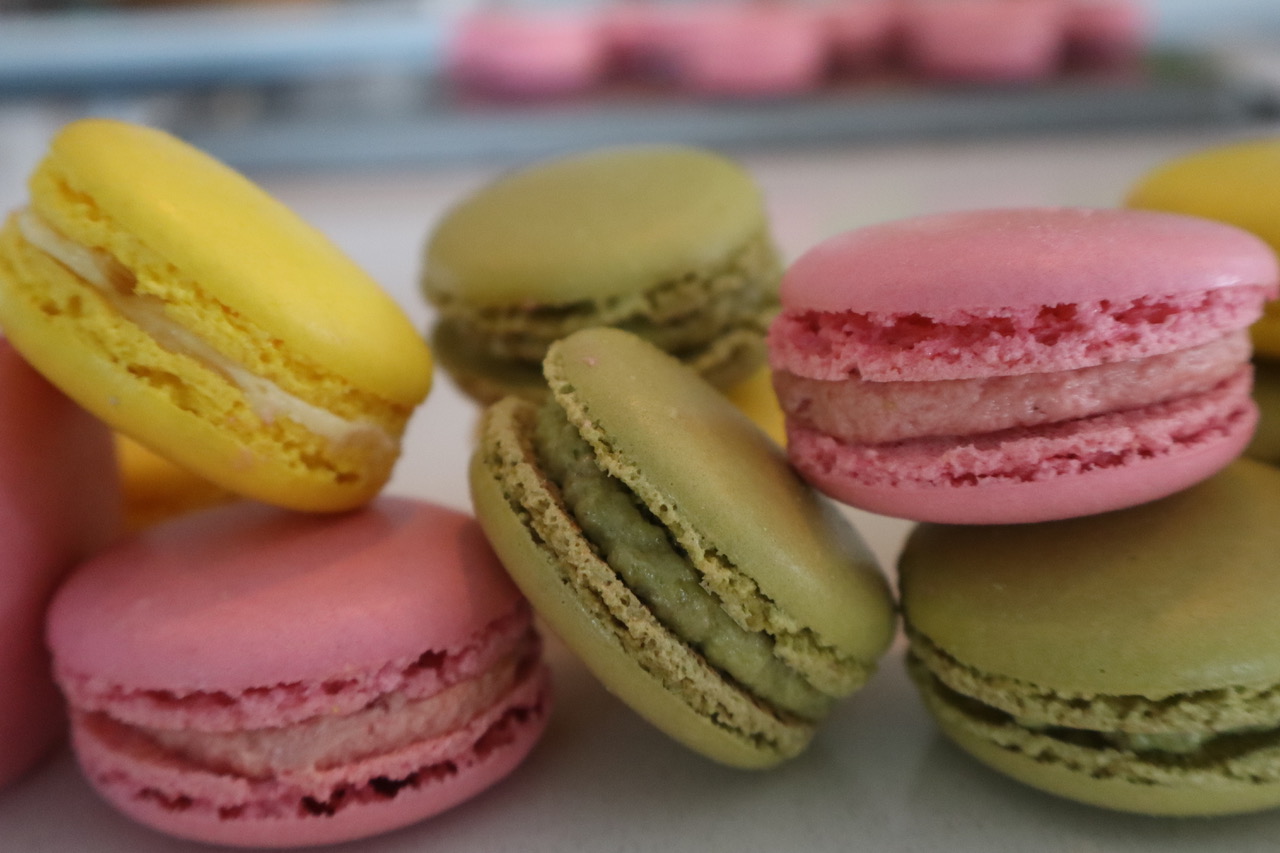 A row of freshly baked macarons in soft yellow, pistachio, and rose